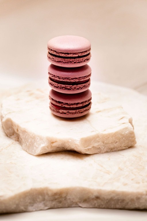 Trois macarons roses empilés sur une pierre blanche aux bords irréguliers.