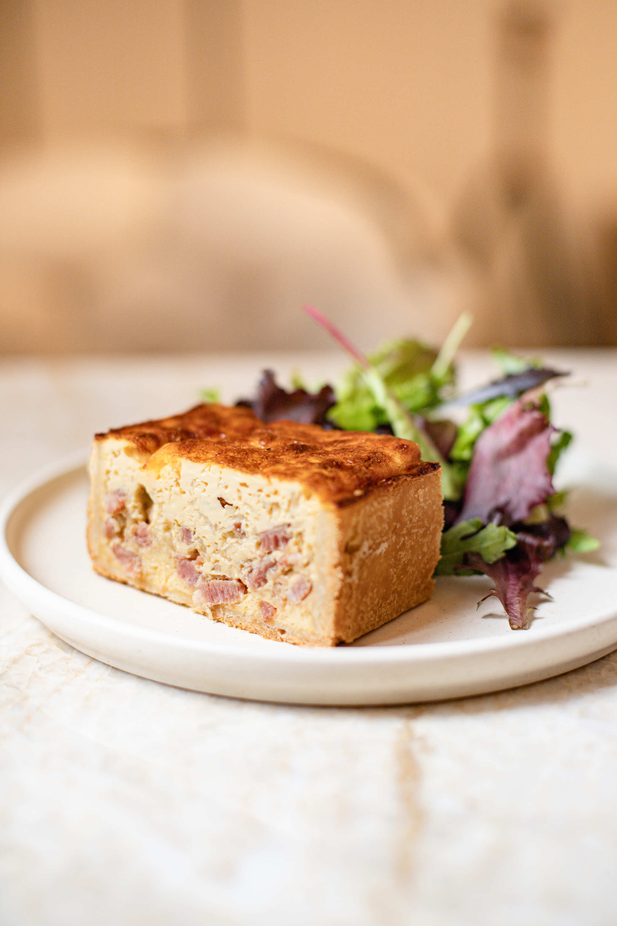Tranche de quiche aux morceaux de jambon servie avec salade verte sur assiette blanche