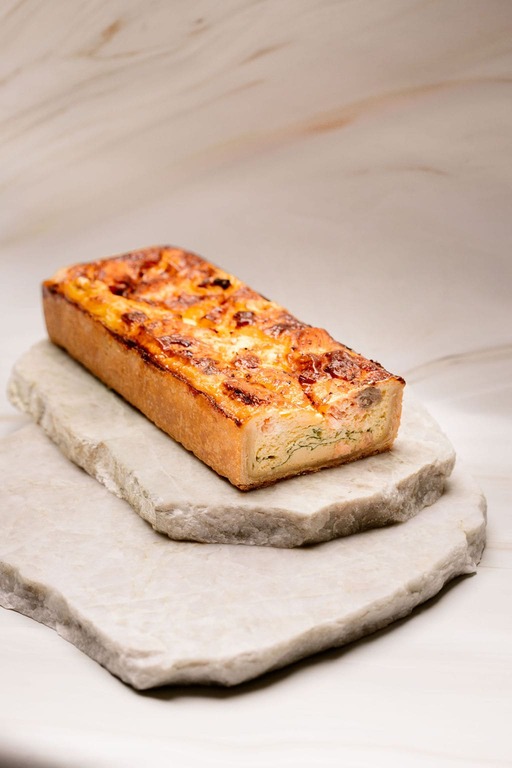 Gâteau salé rectangulaire au fromage gratiné sur deux plaques de pierre empilées.