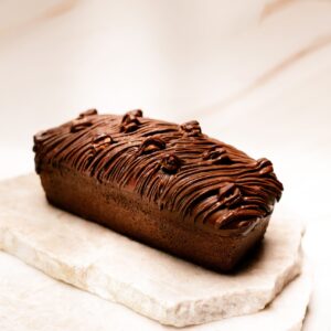 Gâteau rectangulaire au chocolat avec glaçage orné de volutes, posé sur plaques de marbre blanc.