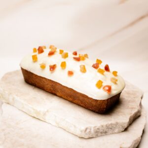 Cake rectangulaire glacé blanc avec morceaux de fruits confits sur une plaque en pierre.