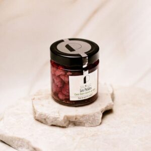 Pot en verre fermé contenant des cerises rouges sur deux plaques de pierre blanche.