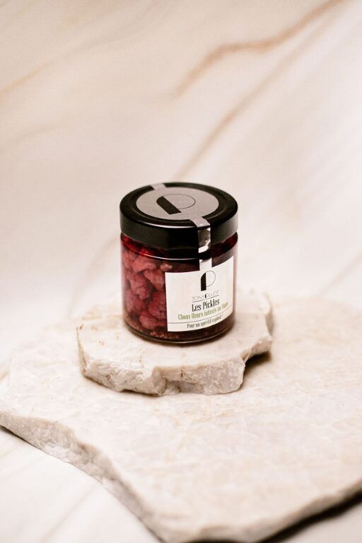 Pot en verre fermé contenant des cerises rouges sur deux plaques de pierre blanche.