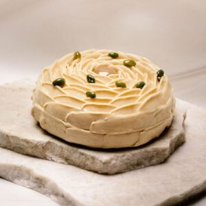 Pâtisserie ronde beige décorée en spirale avec petites graines vertes sur plaques de pierre.