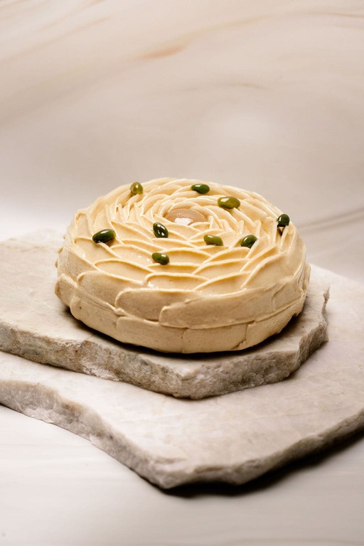 Pâtisserie ronde beige décorée en spirale avec petites graines vertes sur plaques de pierre.