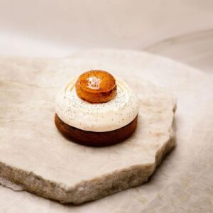 Dessert rond avec base brune, crème blanche parsemée de petites particules noires et dôme caramelisé brillant.