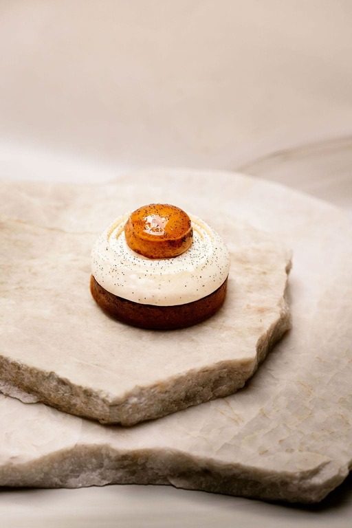 Dessert rond avec base brune, crème blanche parsemée de petites particules noires et dôme caramelisé brillant.