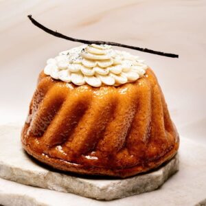 Cake glacé rond cannelé, décor crème fouettée en pétales et gousse de vanille, sur deux plaques marbre.