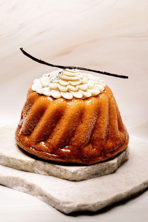 Cake glacé rond cannelé, décor crème fouettée en pétales et gousse de vanille, sur deux plaques marbre.