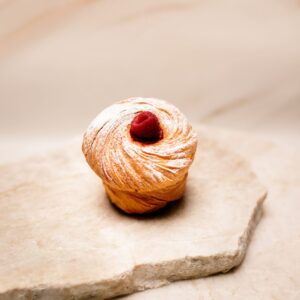 Gâteau feuilleté rond saupoudré de sucre glace avec une framboise sur un support en pierre beige.