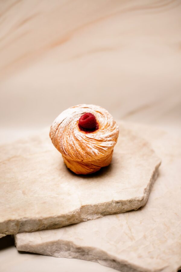 Gâteau feuilleté rond saupoudré de sucre glace avec une framboise sur un support en pierre beige.