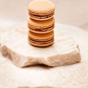 Trois macarons marron clair empilés sur une surface de pierre beige texturée.