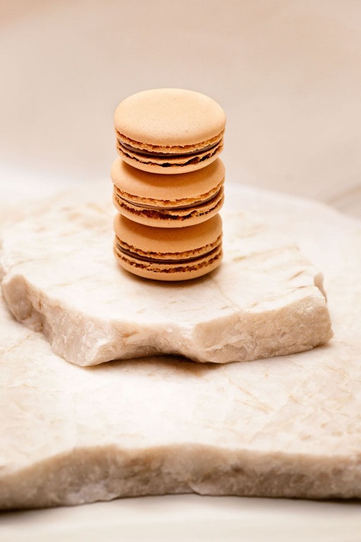 Trois macarons marron clair empilés sur une surface de pierre beige texturée.