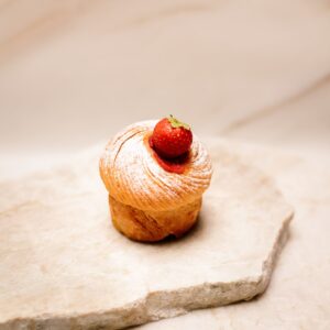 Petit gâteau feuilleté saupoudré de sucre glace avec une fraise sur des pierres claires.