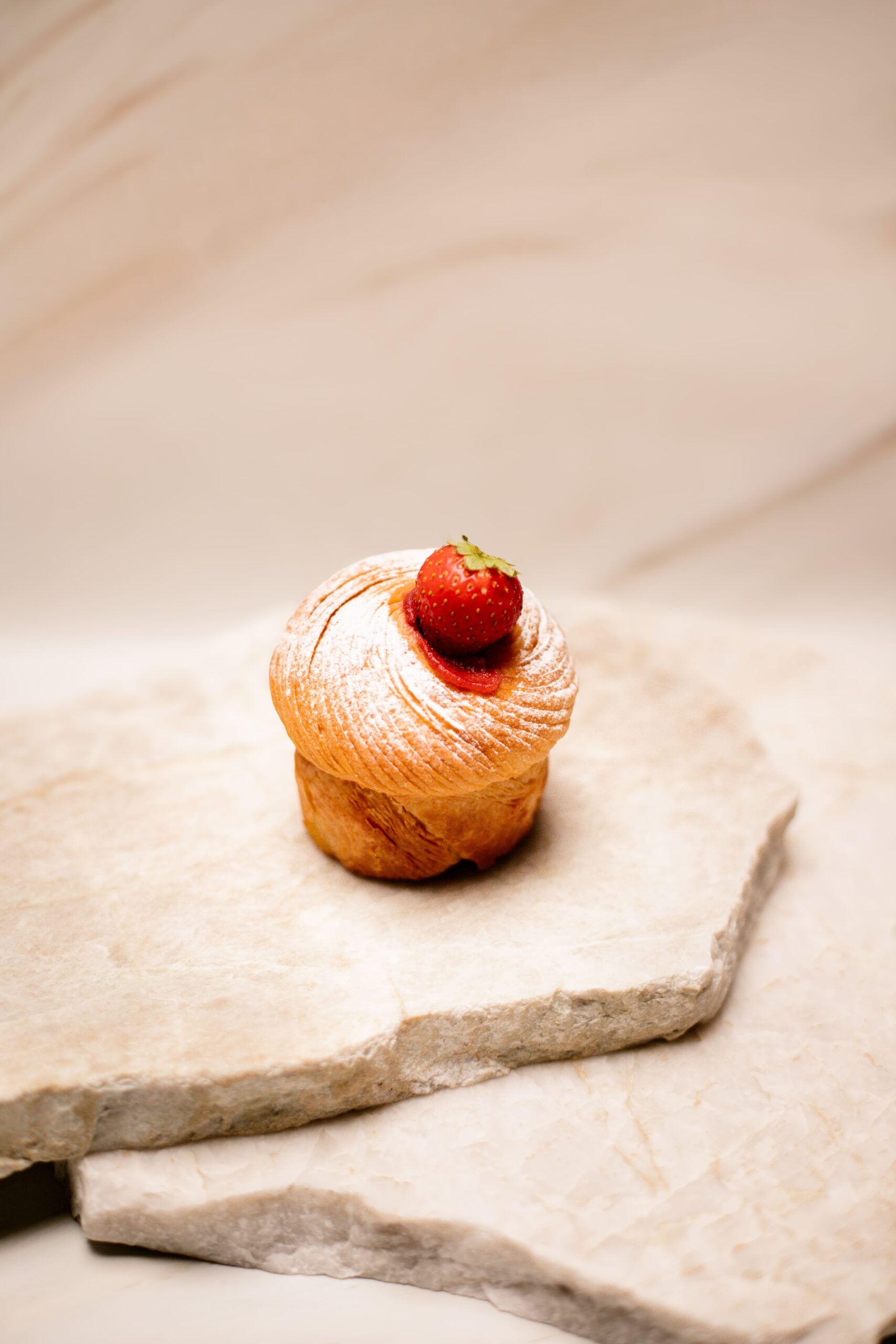 Petit gâteau feuilleté saupoudré de sucre glace avec une fraise sur des pierres claires.
