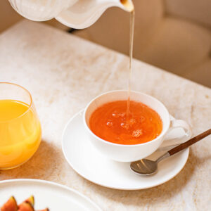 Versement de thé dans une tasse blanche avec un verre de jus d'orange et une pâtisserie aux figues.