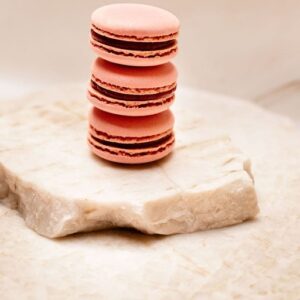 Trois macarons roses empilés sur une plaque de pierre claire aux bords irréguliers.