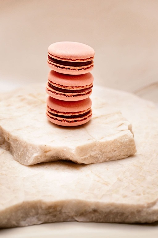 Trois macarons roses empilés sur une plaque de pierre claire aux bords irréguliers.