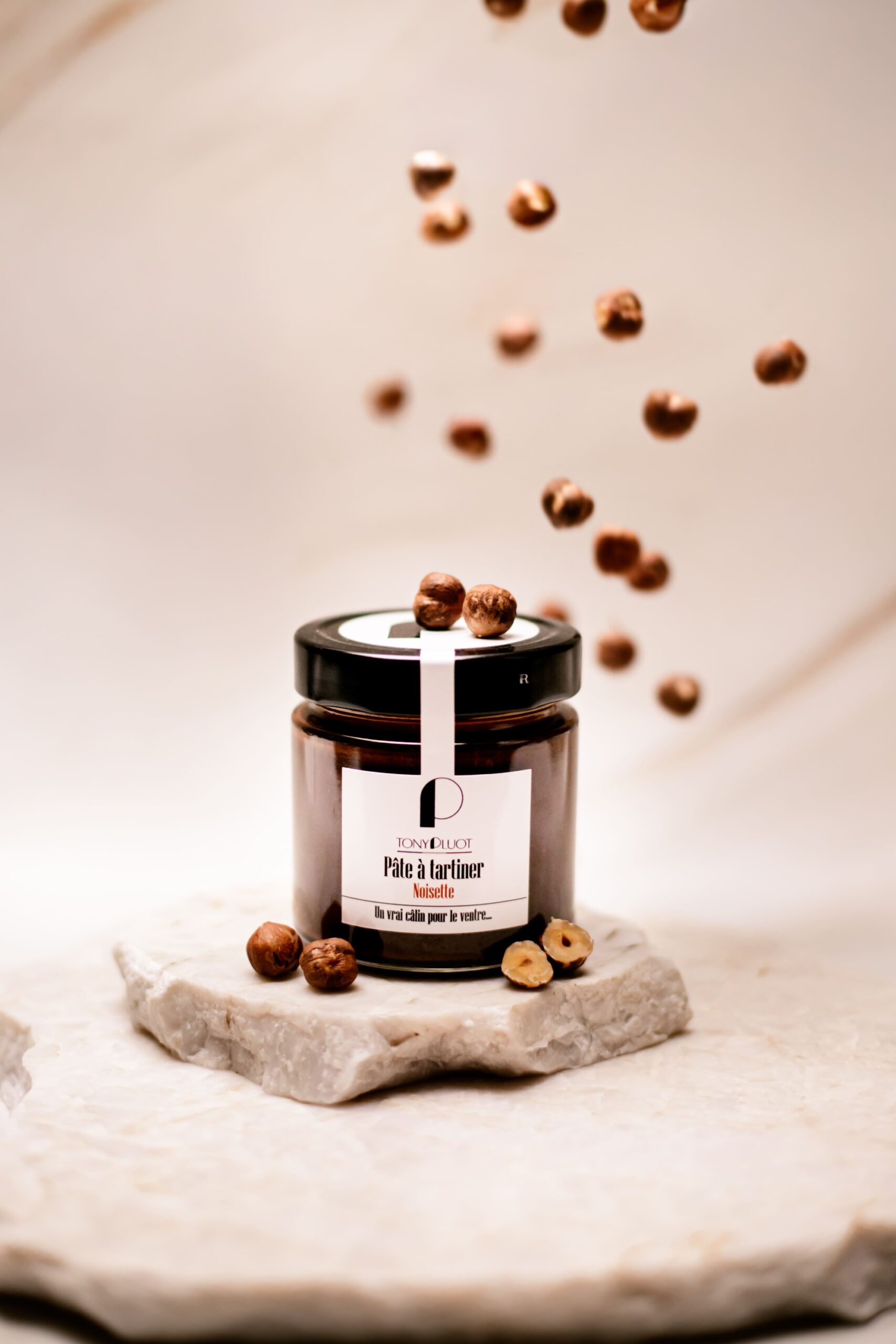 Pot de pâte à tartiner noisette Tony Pluot sur pierre avec noisettes entières autour.