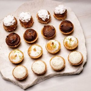 Petites tartes variées alignées sur une plaque en pierre avec différentes garnitures.
