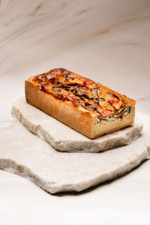 Tarte rectangulaire aux légumes variés sur pâte épaisse posée sur deux plaques de pierre.