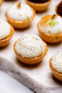 Tartelettes à la crème blanche et zestes verts posées sur un plateau en marbre blanc.