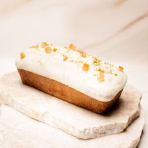 Gâteau rectangulaire glacé blanc décoré d'agrume confit et zestes verts sur pierres.