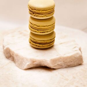 Trois macarons jaunes empilés sur une plaque de pierre beige claire.