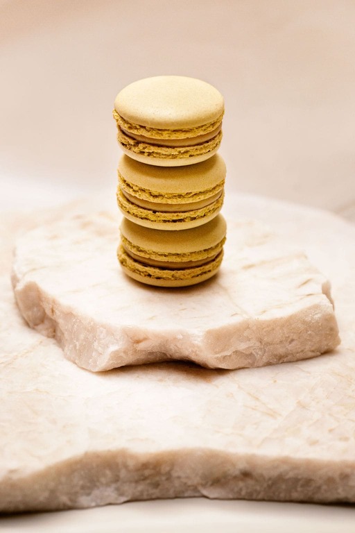 Trois macarons jaunes empilés sur une plaque de pierre beige claire.
