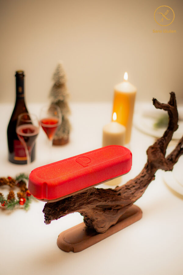 Dessert de Noël sans gluten_en forme de bûche et de capsule de champagne de couleur rouge avec des paillettes dorées sur un support artistique en chocolat sculpté