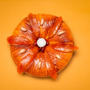 Dessert en forme ronde pour l'Épiphanie, pâte feuilletée inversée, frangipane amande et clémentines corses, fève en céramique sur fond orange