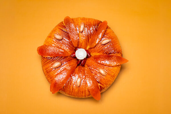 Dessert en forme ronde pour l'Épiphanie, pâte feuilletée inversée, frangipane amande et clémentines corses, fève en céramique sur fond orange