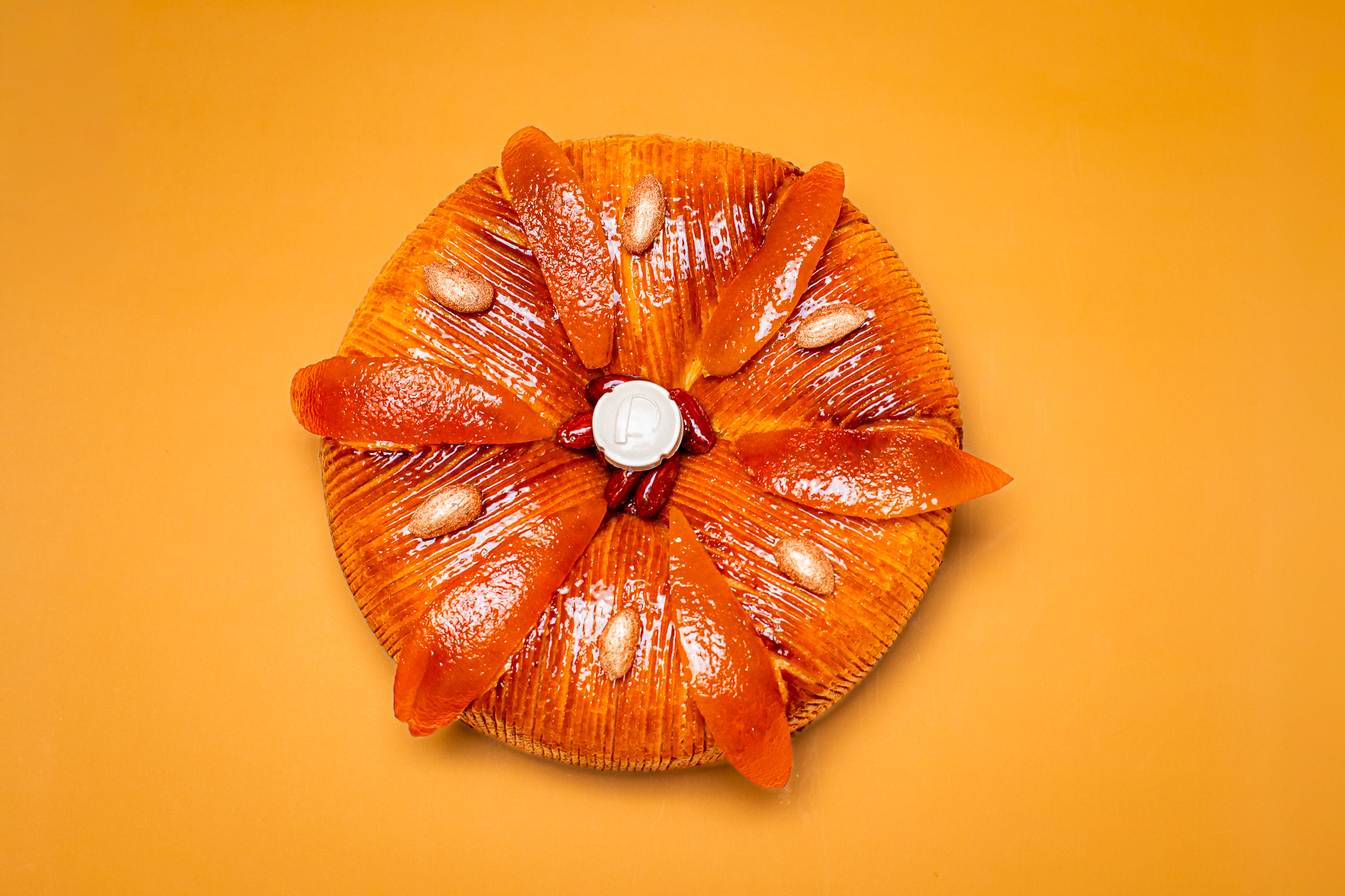 Dessert en forme ronde pour l'Épiphanie, pâte feuilletée inversée, frangipane amande et clémentines corses, fève en céramique sur fond orange