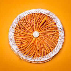 Dessert en forme ronde pour l'Épiphanie, pâte feuilletée inversée, frangipane amande avec fève en céramique sur fond orange