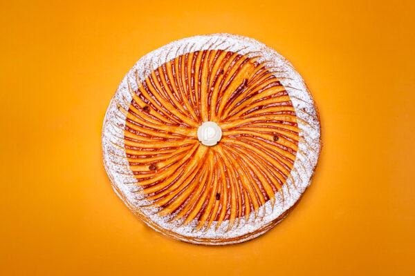 Dessert en forme ronde pour l'Épiphanie, pâte feuilletée inversée, frangipane amande avec fève en céramique sur fond orange