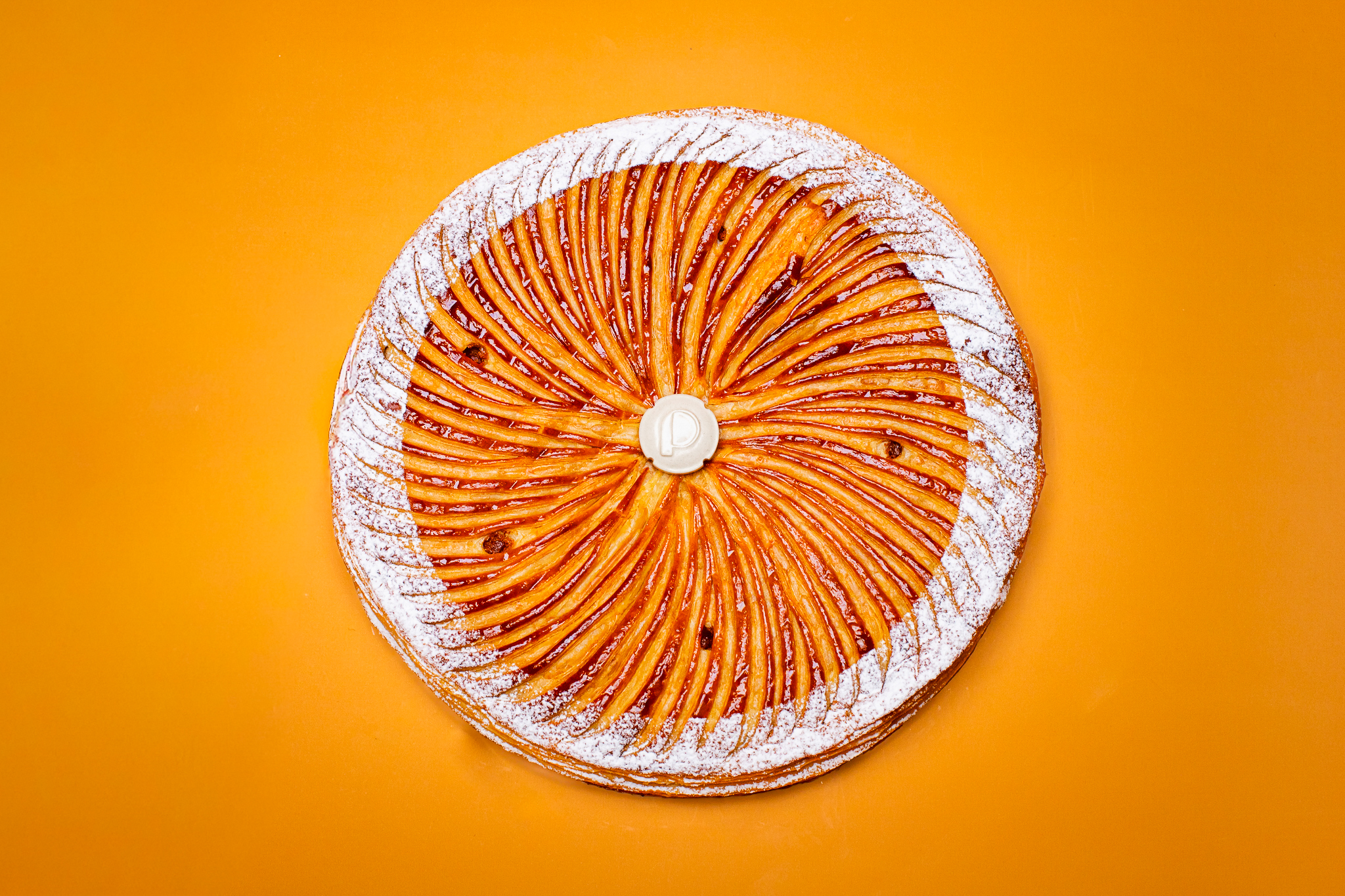 Dessert en forme ronde pour l'Épiphanie, pâte feuilletée inversée, frangipane amande avec fève en céramique sur fond orange