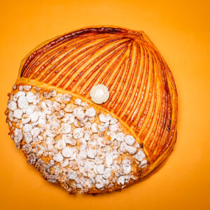 Dessert en forme ronde pour l'Épiphanie, pâte feuilletée inversée, frangipane noisette du Piémont avec fève en céramique sur fond orange