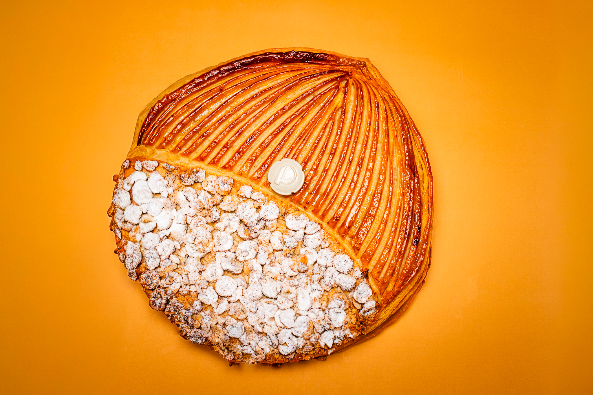 Dessert en forme ronde pour l'Épiphanie, pâte feuilletée inversée, frangipane noisette du Piémont avec fève en céramique sur fond orange