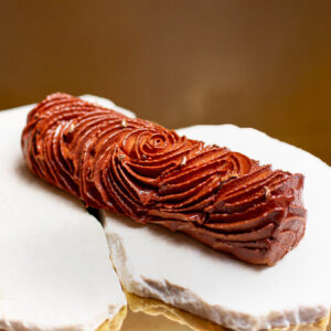 Dessert de Noël sans gluten en forme de bûche de couleur chocolat avec des paillettes dorées posée sur marbre et un fond doré