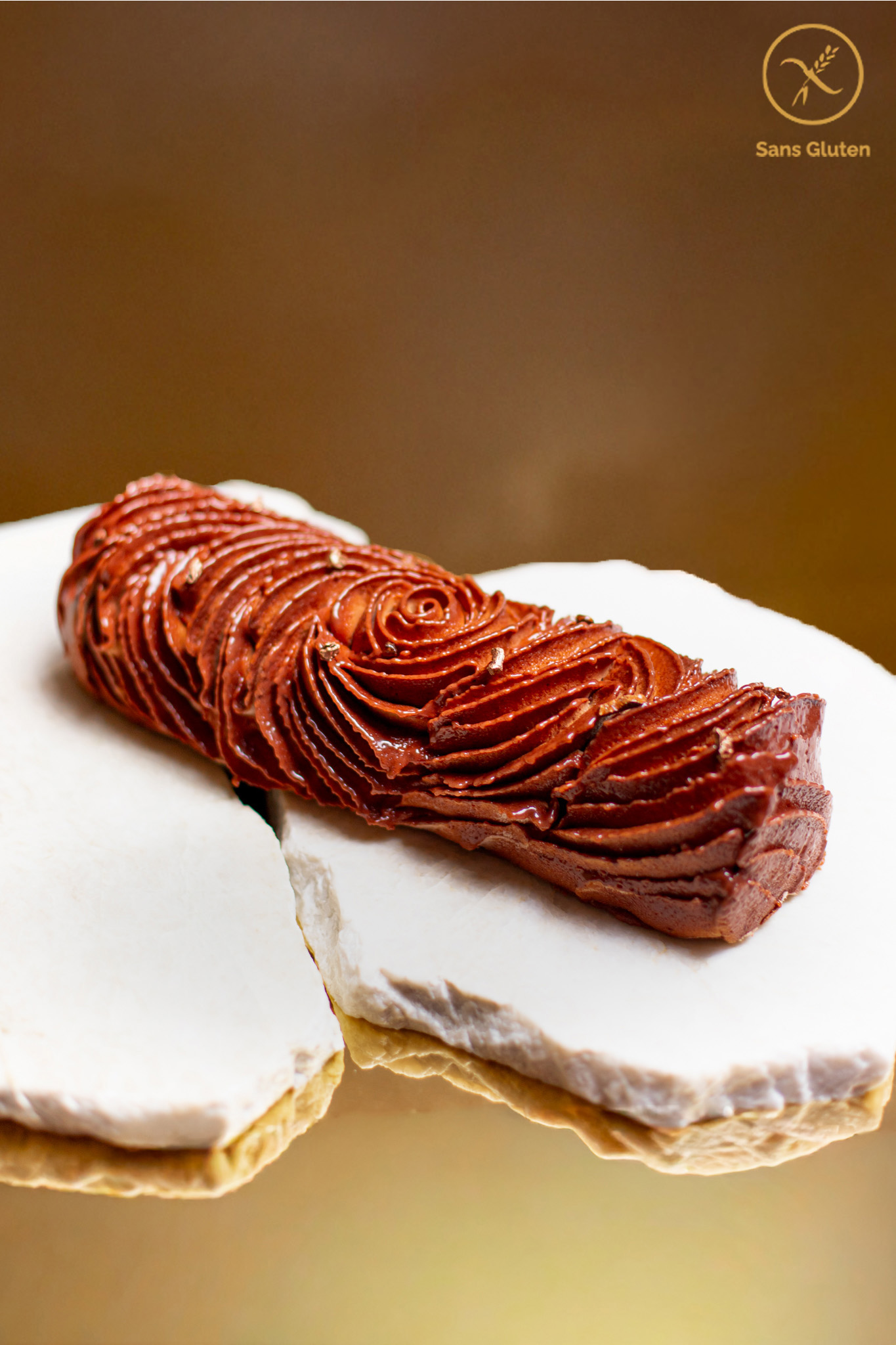 Dessert de Noël sans gluten en forme de bûche de couleur chocolat avec des paillettes dorées posée sur marbre et un fond doré
