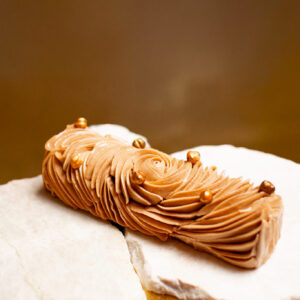 Dessert de Noël sans gluten en forme de bûche de couleur chocolat avec des paillettes dorées posée sur marbre et un fond doré