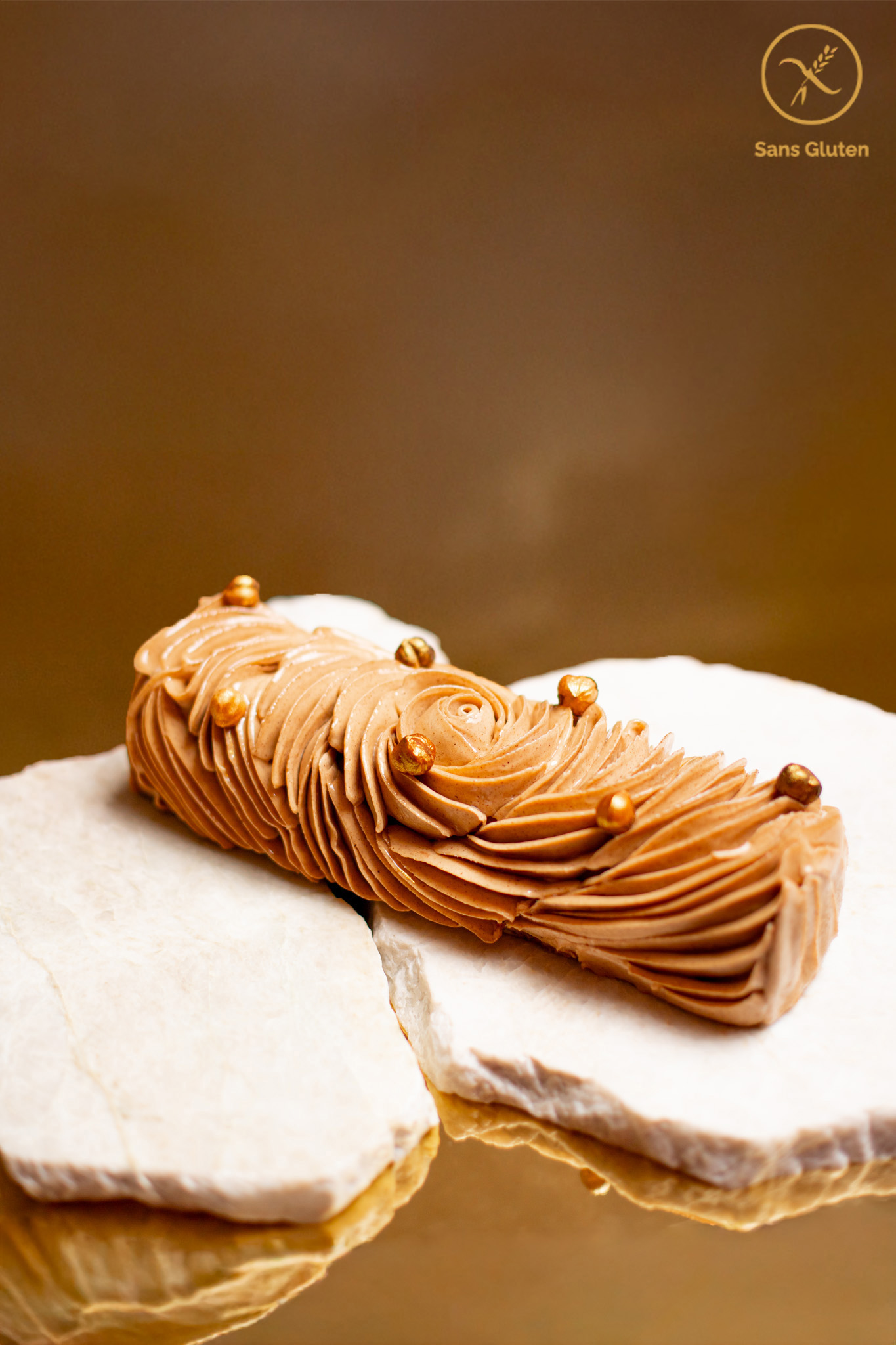 Torino_Sans GlutenTony Pluot Dessert de Noël sans gluten en forme de bûche de couleur chocolat avec des paillettes dorées posée sur marbre et un fond doré