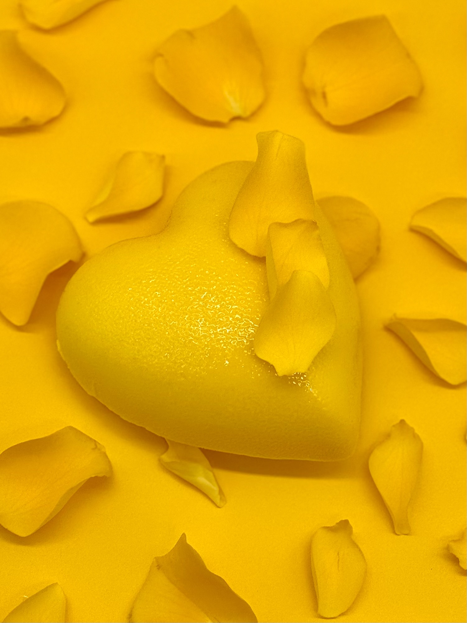 Sur un fond jaune, un gateau en forme de cœur jaune avec de pétales jaunes pour la Saint-Valentin