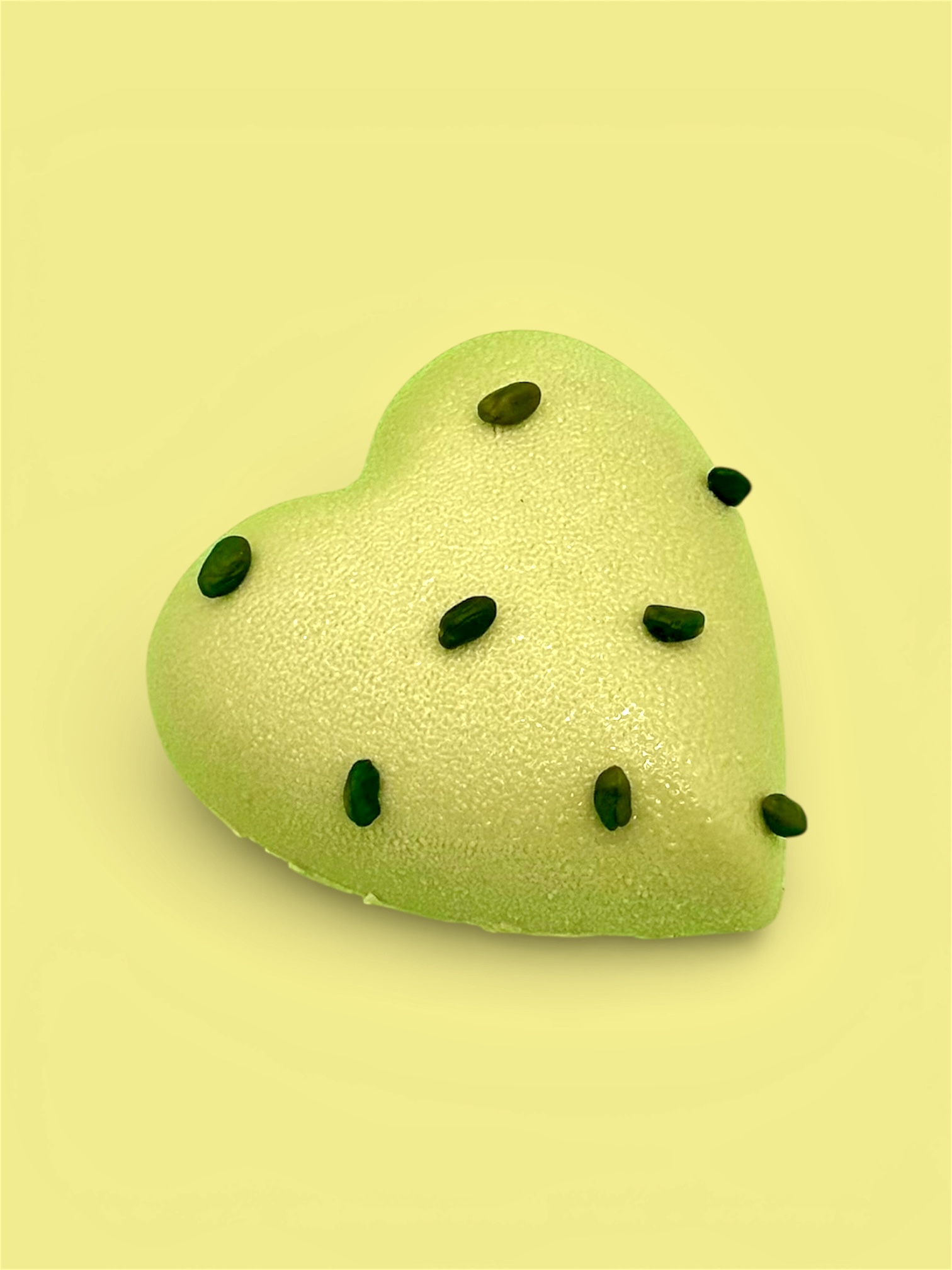 Sur un fond vert, un gateau en forme de coeur pistache avec des pistaches concassées pour la Saint-Valentin