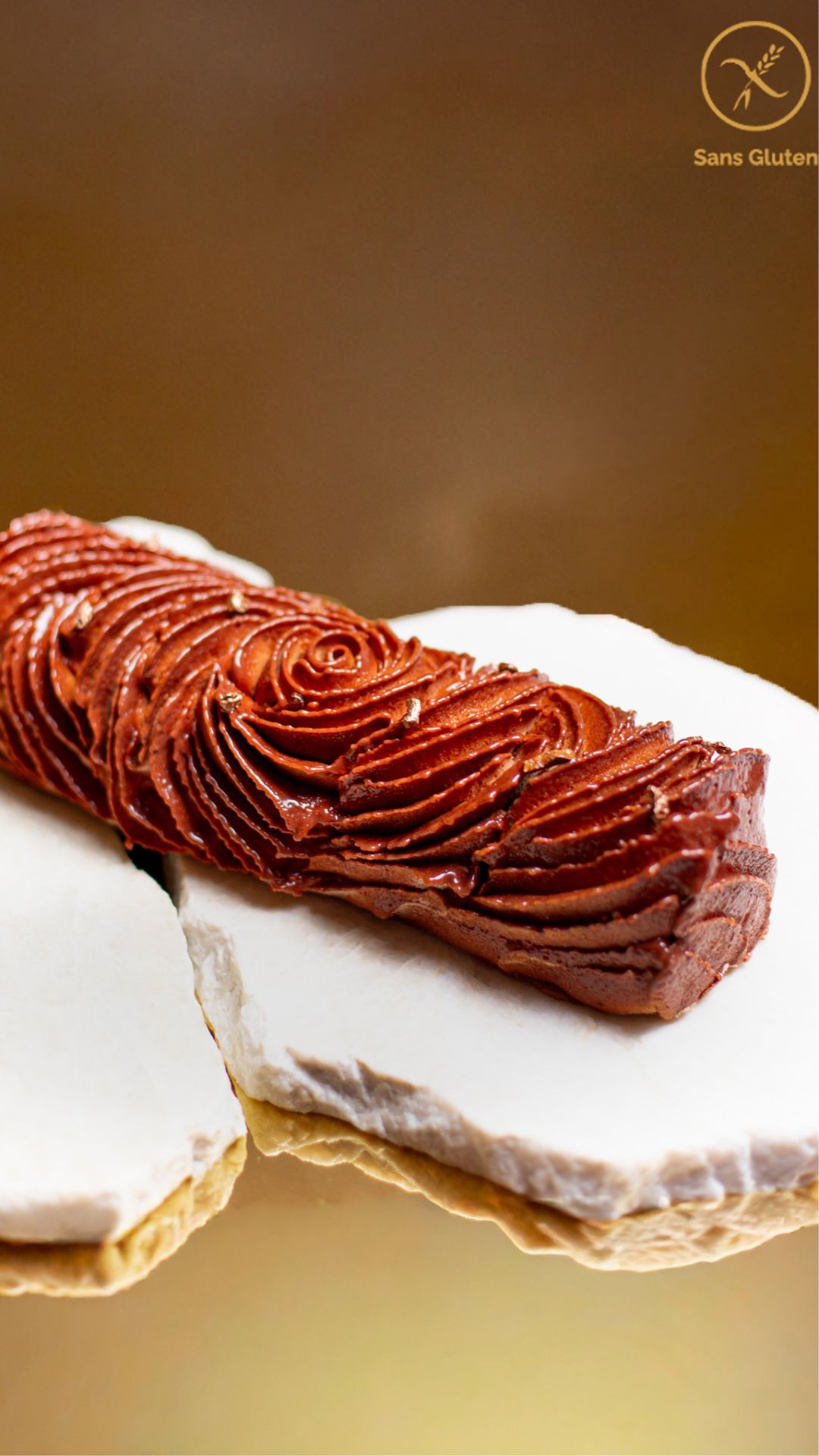 Dessert de Noël sans gluten en forme de bûche de couleur chocolat avec des paillettes dorées posée sur marbre et un fond doré