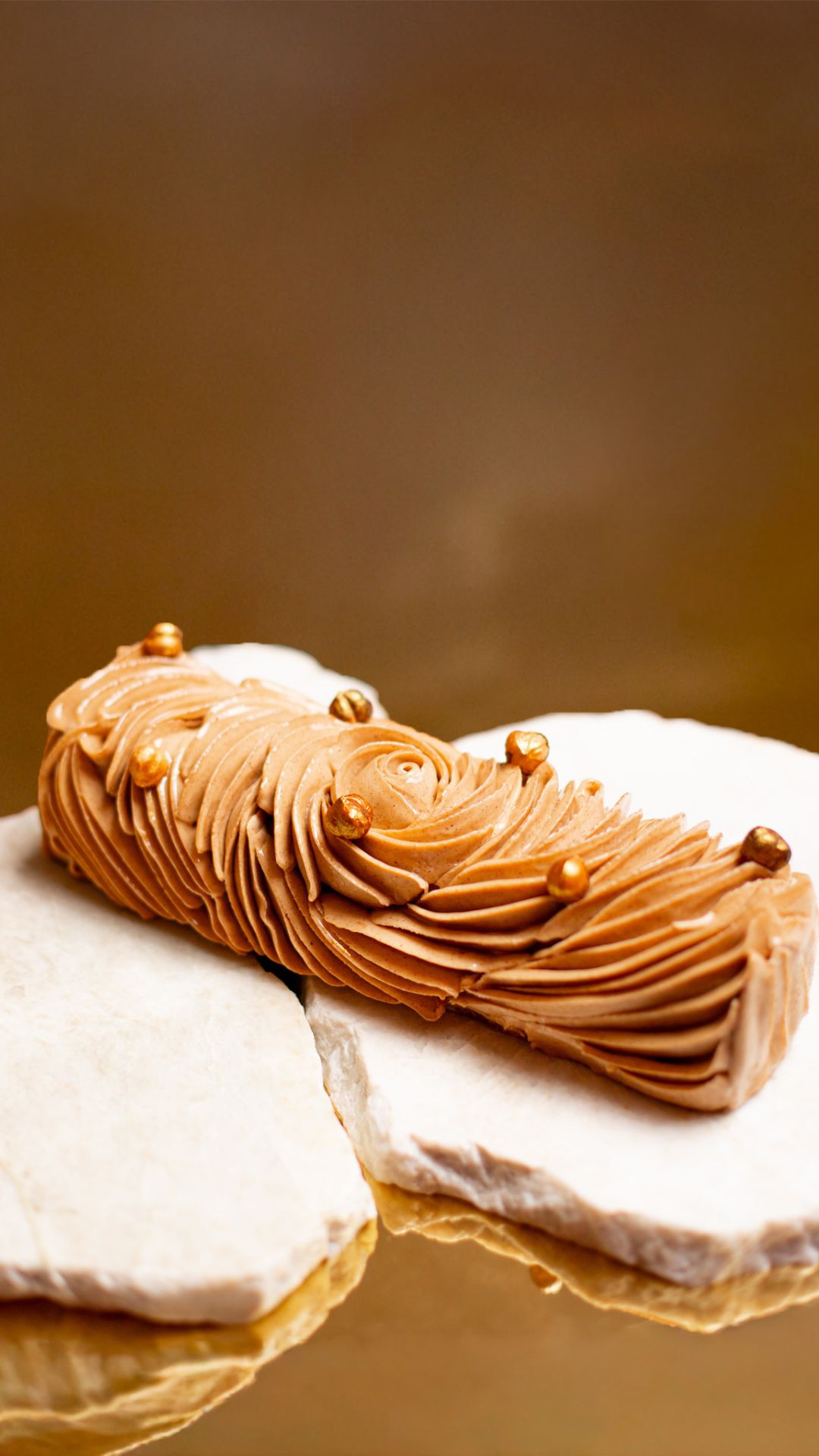 Dessert de Noël sans gluten en forme de bûche de couleur chocolat avec des paillettes dorées posée sur marbre et un fond doré